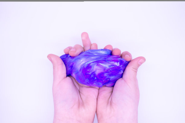 白色背景下，有人手里拿着蓝粉两色的黏液。黏液被手压碎、拉伸、撕裂和挤压图片下载