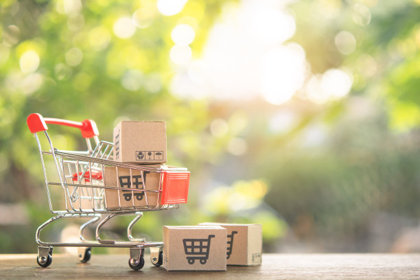 购物概念-购物车或手推车和纸盒或包裹与购物车标志的木桌子。网上购物的消费者可以在家购物和送货服务。与复制空间图片下载