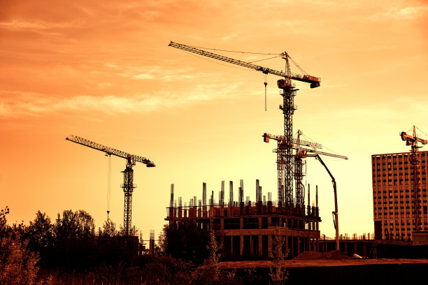 在黄桔色的天空下，建筑工地的塔吊和建筑轮廓图片下载