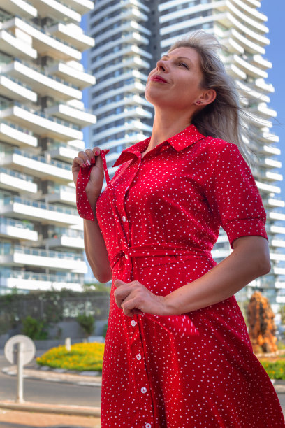 一个穿着红衣服的年轻漂亮女孩站在高楼大厦的背景下图片下载