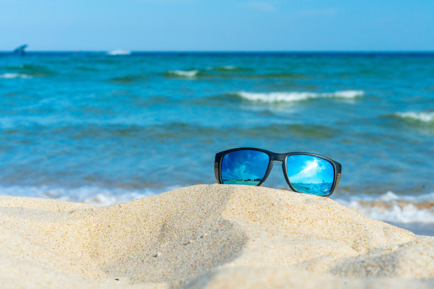 太阳镜躺在沙滩上，蓝色的海浪为背景。休闲，假期，假期，夏天的概念。波兰波罗的海。图片下载