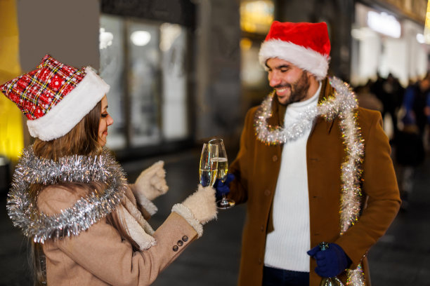 一对戴着圣诞帽的年轻夫妇在城市的街道上饮酒作乐。图片下载