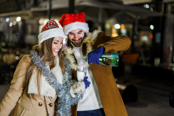 快乐的年轻夫妇带着圣诞礼物走在城市的街道上，喝着酒敬酒。图片下载