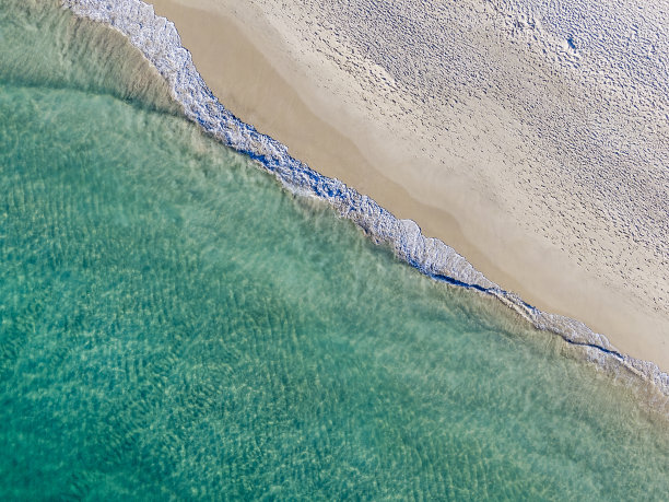 鸟瞰图，正上方，对角线温和的蓝绿色波浪打破白色的沙滩上的脚印图片下载