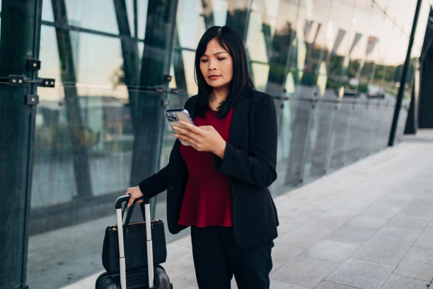 她一边推着行李箱，一边全神贯注地看着智能手机上的东西图片下载