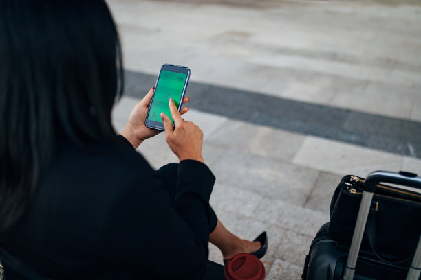 后视图的商业妇女使用智能手机与绿色屏幕，而坐在长凳上图片下载