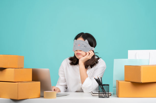 年轻的女人累了，伤心了，筋疲力尽了。商务亚洲女性穿衬衫坐在白色的办公桌上工作与pc笔记本电脑和棕色纸箱孤立在绿色的背景。图片下载