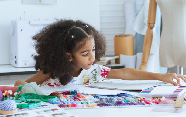 可爱的非洲小女孩在裁缝室在纸上画或素描服装设计，舒适的家是她的职业梦想，微笑着幸福和乐趣。休闲，生活方式，教育，儿童概念。图片下载