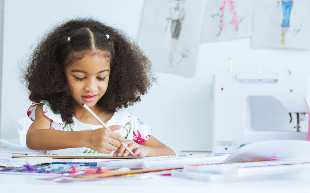 可爱的非洲小女孩在裁缝室在纸上画或素描服装设计，舒适的家是她的职业梦想，微笑着幸福和乐趣。休闲，生活方式，教育，儿童概念。图片下载
