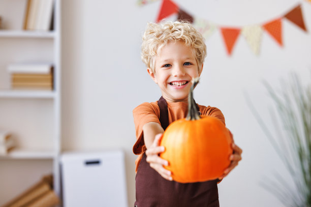 在万圣节庆祝活动中，微笑的小男孩笑着拿着南瓜图片下载