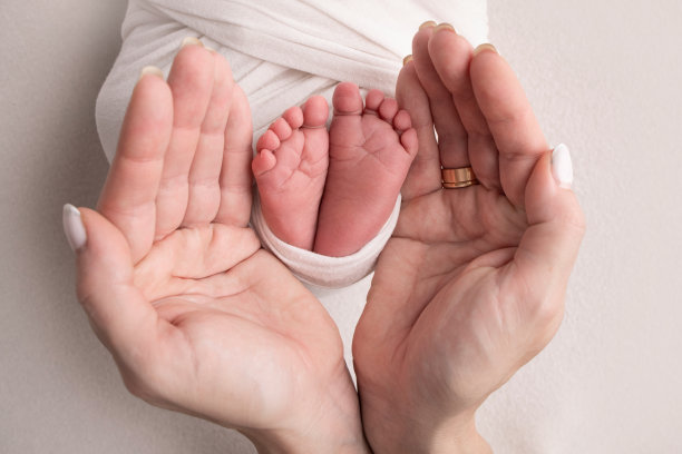 父母的手掌。一位母亲抱着新生儿的脚，婴儿裹在白色的毯子上，背景是白色。新生儿的脚在父母的手中。脚、鞋跟和脚趾的照片图片下载