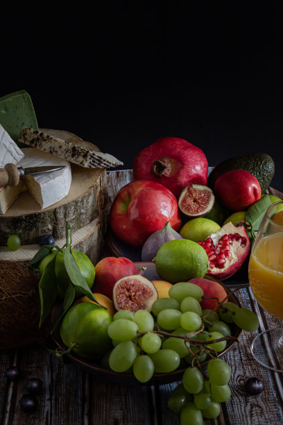 提供葡萄，橘子，无花果，油桃，蓝莓，牛油果，橘子，酸橙和一杯天然的新鲜果汁与各种各样的奶酪放在一个木制的乡村桌子上。深色穆迪概念艺术照片。图片下载
