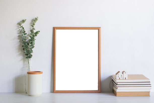 木质相框，绿色的树叶，书籍和白色墙壁上的迷你房子，自然光线。图片下载
