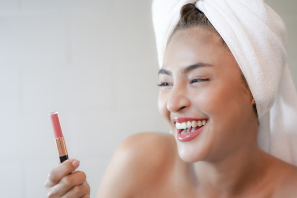穿着白毛巾的年轻女子展示着口红。图片下载