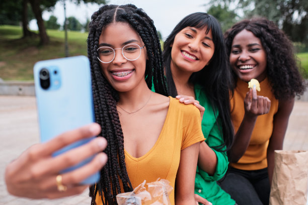 一名年轻女子在公园里和朋友们一边吃薯片一边自拍图片下载