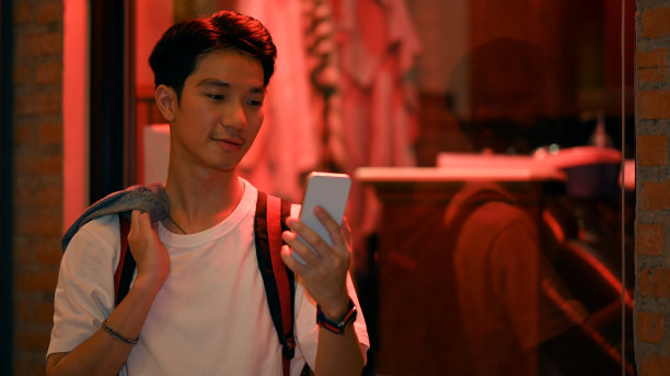 英俊的潮人站在霓虹灯下，在夜晚的城市街道上打字短信。图片下载