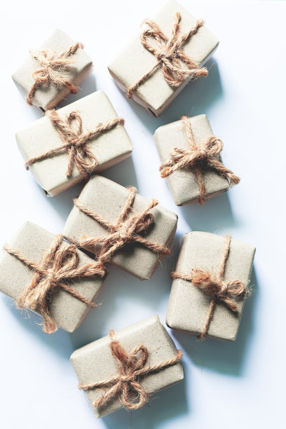 白色背景的棕色礼品盒。一套手工制作的礼物，牛皮纸，用宽麻绳扎，白色桌子上装饰着干花。俯视图图片下载