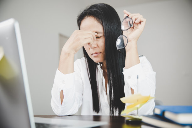 年轻的商业女性人昏昏欲睡，有沮丧的眼睛问题和头痛病，因为使用笔记本电脑在她的办公桌上。压力大的女员工因过度工作而疲惫不堪。图片下载
