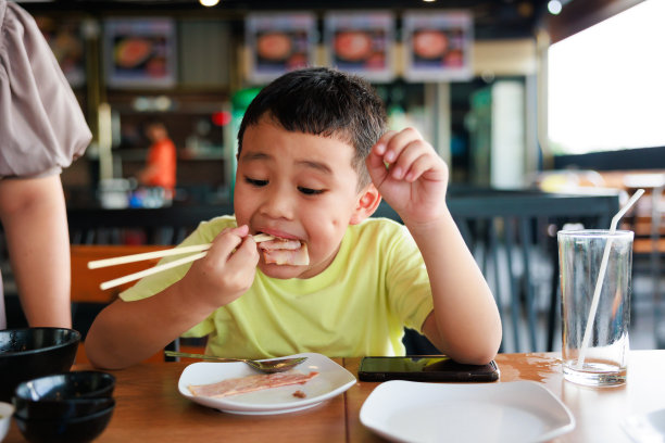 饥饿的亚洲小男孩用筷子吃烤培根，美味的烧烤餐厅。图片下载