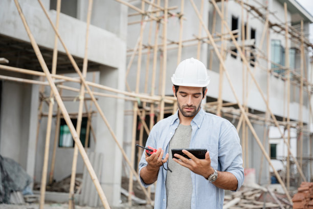 年轻的男工程师站在工地上，用手提收音机交谈，检查各种功能。图片下载