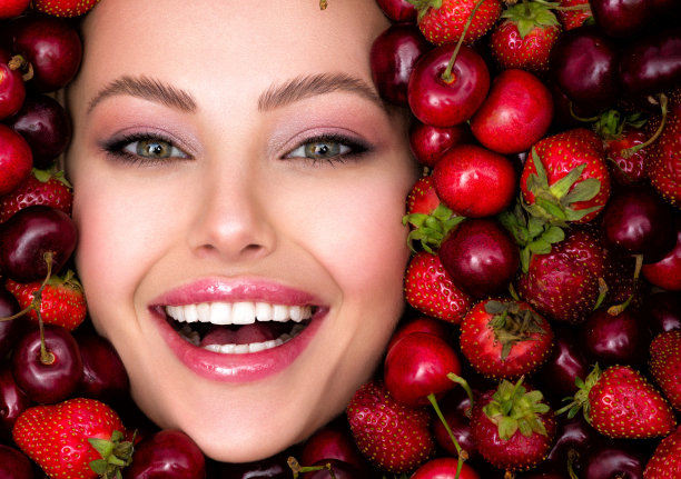 年轻，微笑的女孩，明亮的妆容和浆果背景。迷人的女人，洁白闪亮的牙齿和化妆品。图片下载
