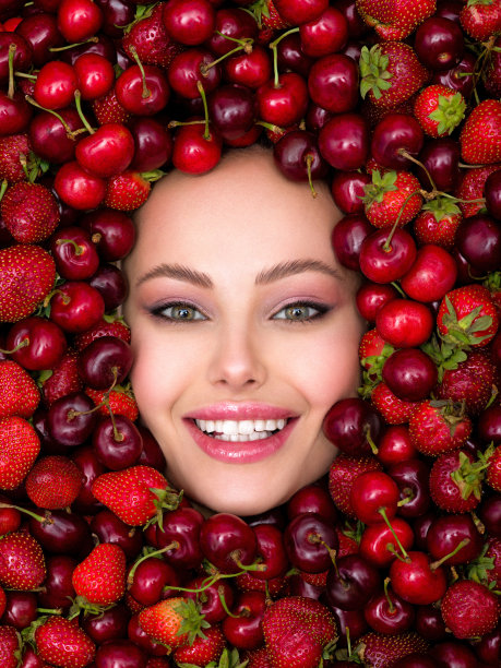 年轻，微笑的女孩，明亮的妆容和浆果背景。迷人的女人，洁白闪亮的牙齿和化妆品。图片下载