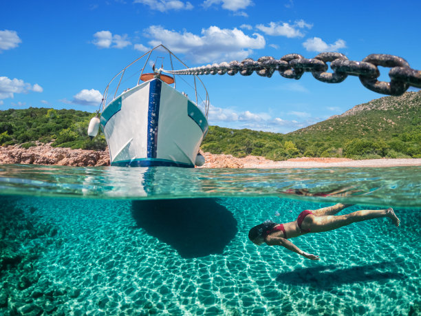 女潜水员正在美丽的海滩上浮潜。照片的下半部分是海底，上半部分是海岸，有一艘游艇和美丽的天空。图片下载