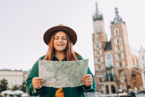 迷人的年轻女游客正在探索新的城市。在克拉科夫市场广场上，红发女孩手持纸质地图。秋天去欧洲旅游。圣玛丽教堂图片下载