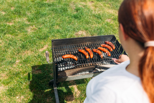 铸铁烤架上的烤猪肉香肠。年轻女子的手在烤肉。年轻的女性在烧烤，年轻的女孩在户外准备食物图片下载