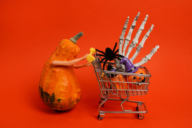 橙色的南瓜手拿着购物车和万圣节装饰的红色背景。在万圣节图片下载
