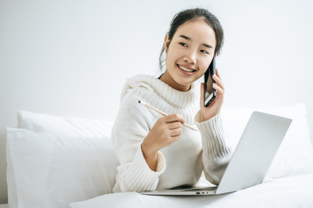 女人一边玩笔记本电脑一边打电话。图片下载