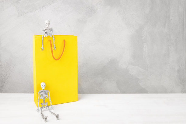 假日购物和万圣节购物。黄色包，深灰色背景上有骷髅，复制空间。图片下载