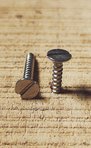 一个螺丝钉的近景微距照片。许多分散的螺丝。其中一个钉在木板上。图片下载