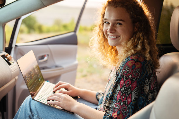 年轻美丽的女商人看着相机在笔记本电脑上工作坐在车里。随时随地学习Ð°。图片下载