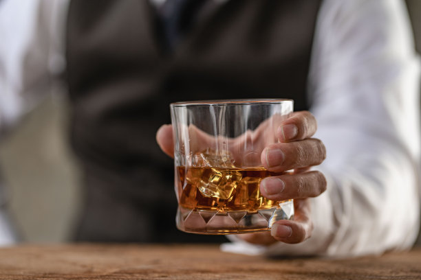 酒保把一杯加冰的威士忌递给男客人。酒吧的其余概念的特写严肃的商人拿着威士忌显示行政特权的概念。图片下载