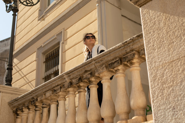 女人的肖像长金发戴着黑色太阳镜，白色毛衣，站在米色大理石栏杆。图片下载