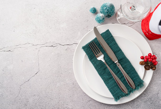 圣诞餐桌设置白色餐具，银器和红色和绿色的装饰在白色的木制背景。前视图。图片下载