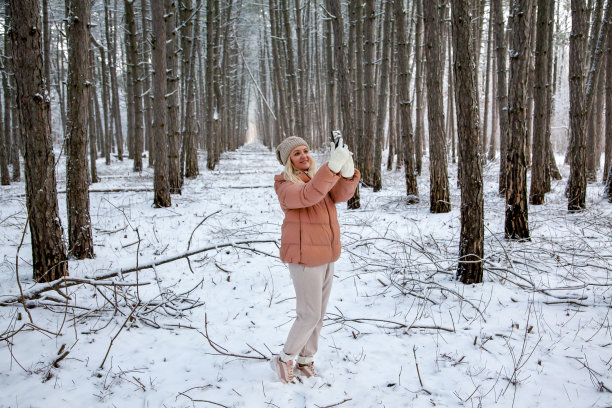 一位年轻女子站在松树林中，用智能手机拍摄大自然的照片图片下载