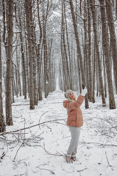 一位年轻女子站在松树林中，用智能手机拍摄大自然的照片图片下载