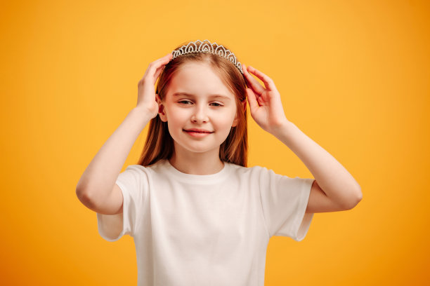 戴着隔离在黄色背景上的王冠的女孩图片下载