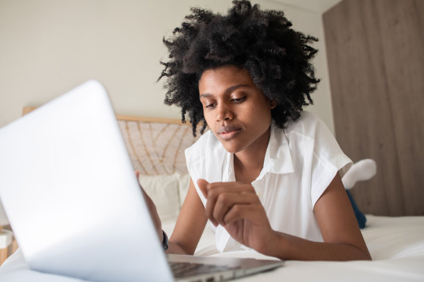 女自由职业者躺在床上，看着笔记本电脑屏幕图片下载