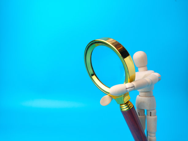 木制假人拿着复古放大镜在蓝色背景与复制空间。图片下载