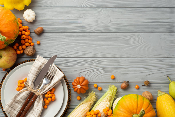 感恩节的概念。俯视图照片的盘子刀叉餐巾南瓜苹果pattypans玉米西葫芦rowan核桃和橡子在孤立的灰色木制桌子背景与空白图片下载