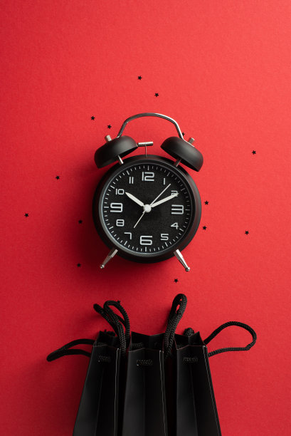 黑色星期五购物概念。俯视图垂直照片黑色闹钟纸袋和纸屑在孤立的红色背景图片下载
