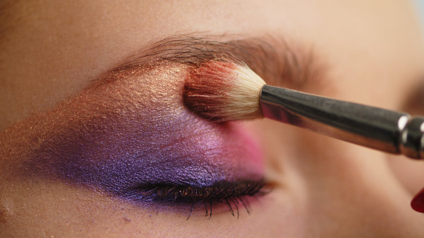 化妆师将化妆品涂在上眼睑上，特写。化妆师用化妆刷涂上明亮的眼影。专业化妆教程大师班。图片下载