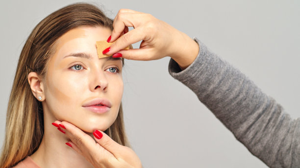 化妆师或造型师用湿海绵在女模特的脸上涂粉底。在脸上涂抹遮瑕膏。图片下载