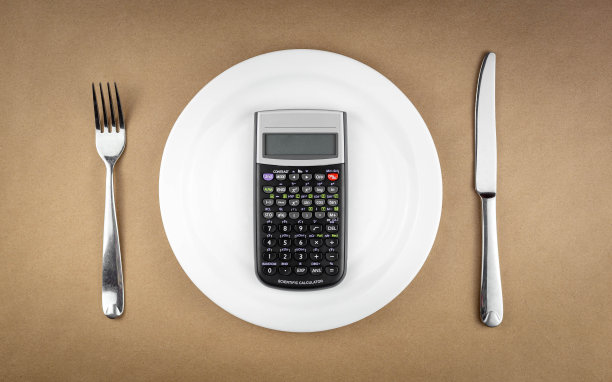 饮食概念计算器在空盘子与叉和刀隔离在棕色再生纸背景图片下载