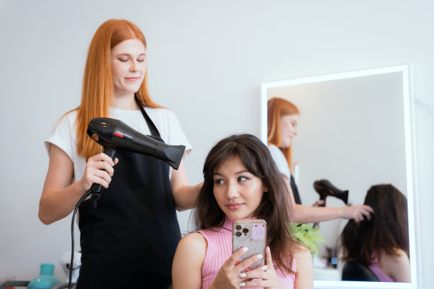 顾客和美容院工作人员正在微笑着交谈。用你的手机来指导你的发型和颜色。图片下载