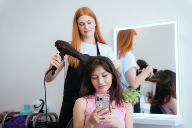 顾客和美容院工作人员正在微笑着交谈。用你的手机来指导你的发型和颜色。图片下载