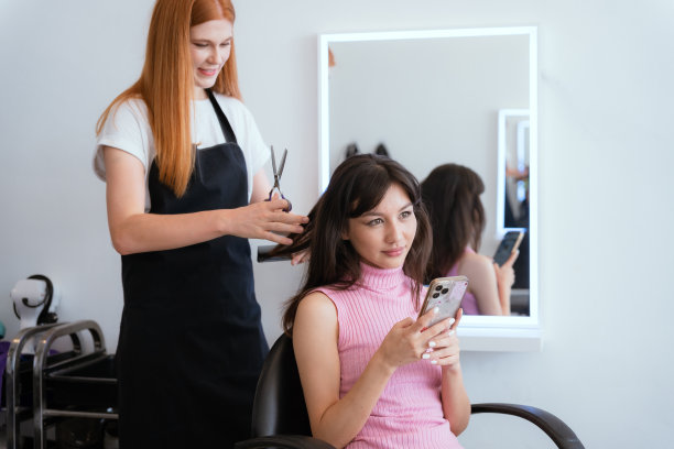 顾客和美容院工作人员正在微笑着交谈。用你的手机来指导你的发型和颜色。图片下载